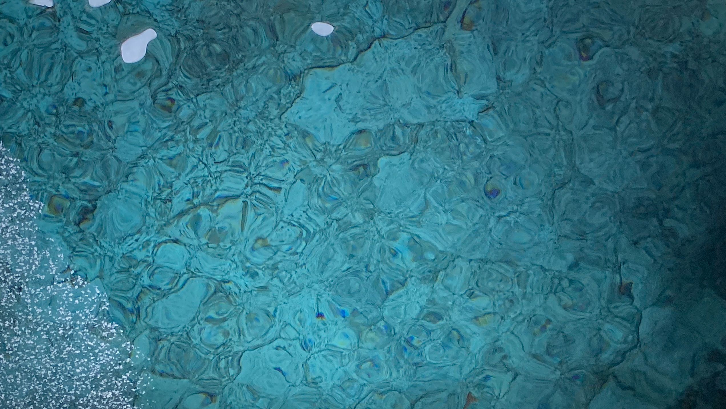 Green-blue water rippling over stones with white surface scum in the top right corner